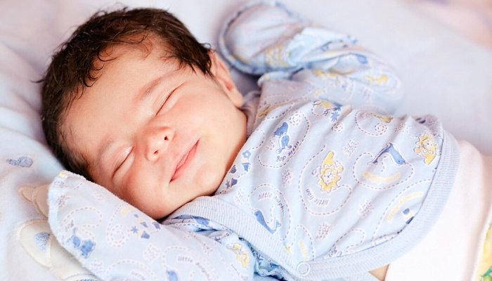 A new baby boy with a full head of hair smiling slightly in his sleep.