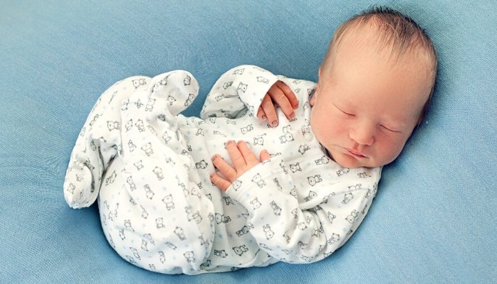 A newborn baby boy with wispy hair lying on a blue blanket.
