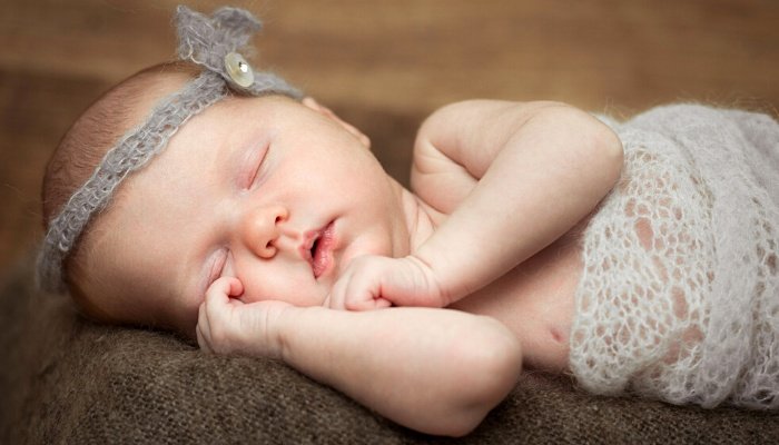 A newborn baby girl posed for a photo shoot wearing a gray headband and blanket.