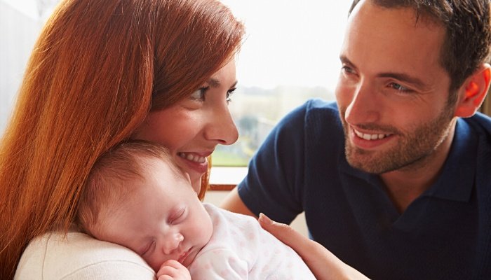 New parents holding their newborn daughter with red hair.