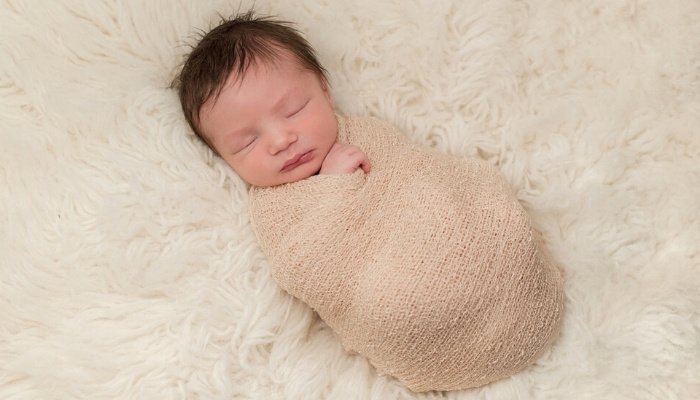 A newborn baby boy sleeping while swaddled tightly.