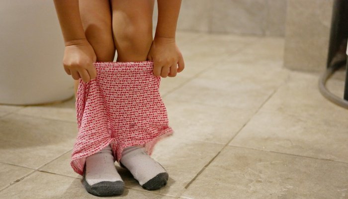 A young girl pulling up her shorts after using the toilet.