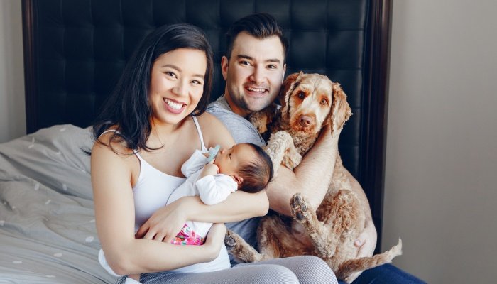 New parents proudly holding their newborn and their Doodle dog.