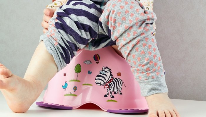 A toddler with her pants pulled down sitting on a child's potty.