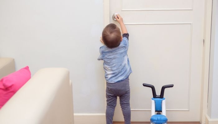 Young toddler boy trying to open the door handle.