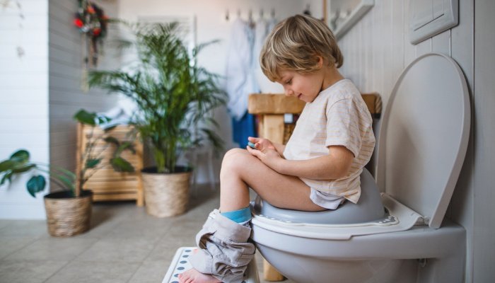 A young boy sitting on the toilet and looking at his phone.