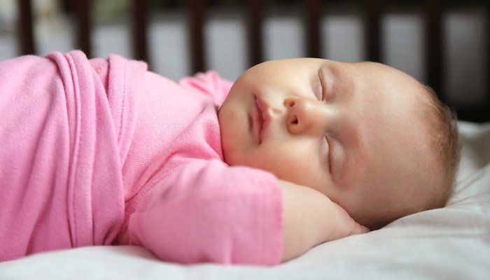 A baby girl in pink pajamas fast asleep in her crib.