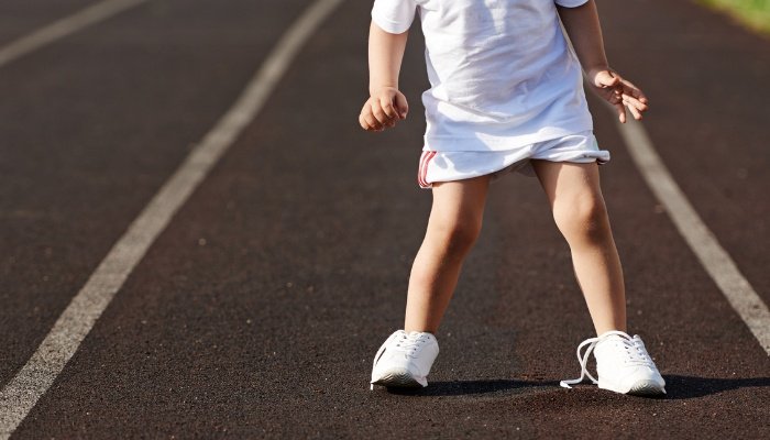 A little girl in a white dress standing on a walking track with one shoe untied.